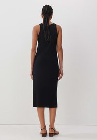 Svart ribbad midiklänning med en figurnära silhuett, ärmlös design och subtil textur. Matchas med bruna sandaler med remmar.
