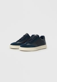 Navy blue sneakers made of leather and suede, featuring a round toe, lace-up design, and a cream-colored rubber sole.