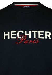 Navyblaue Baumwoll-T-Shirt mit großem weißen Text "HECHTER" und roter Kursive "Paris" auf der Vorderseite. Mit geripptem Kragen.