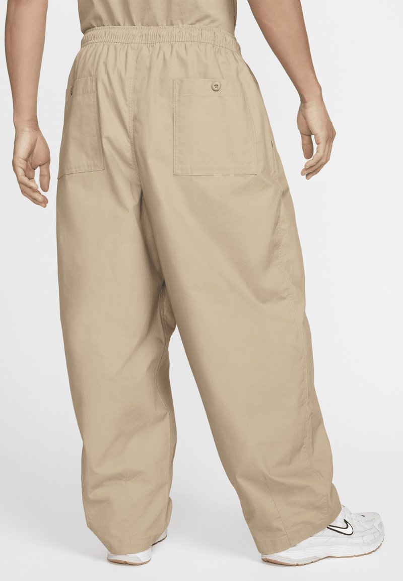 Pantalones cargo beige con una cinturilla elástica, dos bolsillos traseros tipo parche y un corte holgado, combinados con zapatillas blancas.