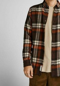 Camicia button-up a quadri nei toni del marrone, crema e arancione. Tessuto morbido con colletto standard e polsini abbottonati, indossata sopra un top beige.