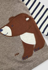 Brun bomulds t-shirt med en bjørn broderi. T-shirten har langærmer i navy og hvid striber, som har bløde teksturer og pæne syninger.