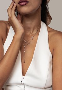 Srebrny naszyjnik z warstwami, posiadający kropliste i okrągłe kamienie szlachetne, noszony z białym topem w stylu halter. Gładka faktura i delikatny design.