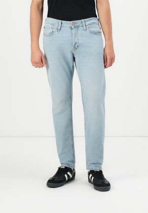 Lys blå denimjeans med rett snitt, fem lommer, beltehemper og en kobberknapp i midjen. Brukt med svarte treningssko.