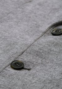 Graues Stoffhemd mit zwei schwarzen Knöpfen, strukturiertem Gewebe und genähtemverschluss, das ein lässiges Design hervorhebt.