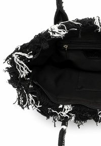 Czarna torba na ramię z teksturowanymi frędzlami i białymi akcentami, wyposażona w kieszeń na zamek oraz gładkie wnętrze. Rączki są plecione.