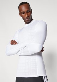 Langärmliges Sportshirt in Weiß, mit einem Gittermuster, tailliertem Design und weicher Textur. Verfügt über einen Rundhalsausschnitt mit flachen Nähten.