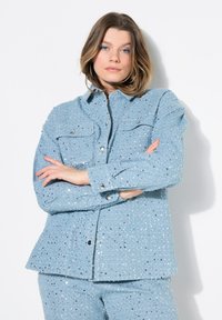 Giacca di paillettes azzurro chiaro con una vestibilità strutturata, dotata di due tasche sul petto e bottoni a scatto, impreziosita da paillettes metalliche testurizzate.