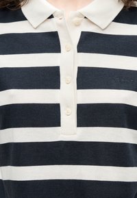 Κοντινό πλάνο μαύρου και λευκού οριζόντιου ριγέ πόλο με λευκό γιακά και τέσσερα κουμπιά στην πατιλέτα.