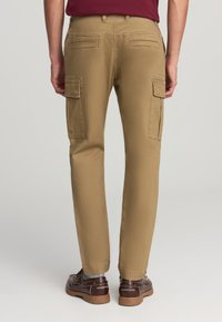Pantaloni cargo beige con vestibilità dritta, dotati di due tasche laterali e due tasche posteriori, realizzati in tessuto di cotone con una superficie liscia.