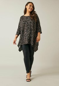 Leopardikuvioinen paita, jossa on kolmanneksen pituiset hihat, virtaava muotoilu, epäsymmetrinen helma, yhdistetty mustiin leggings-housuihin ja mustiin remmikorkokenkiin.