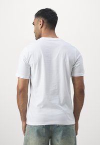 Hvid kortærmet t-shirt, rund halsudskæring, lavet af en bomuldsblanding, glat tekstur, båret med lyseblå denimshorts.