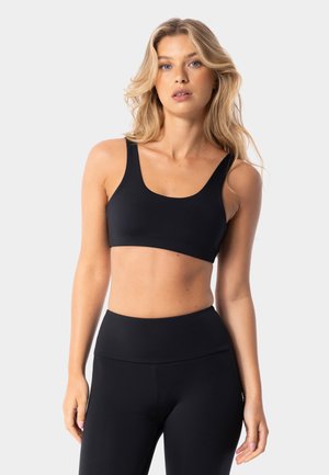 Black athletic bralette with wide straps and a scoop neckline, made of a smooth, stretchy fabric. Paired with high-waisted black leggings.