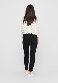 White crocheted sweater with three-quarter sleeves, paired with black fitted jeans and white sneakers. Focus on texture and color contrast.