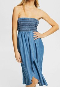 Axelbandslös klänning i denim med en sydd överdel, flödande A-linje kjol och midjekort längd med en lätt volangkant.