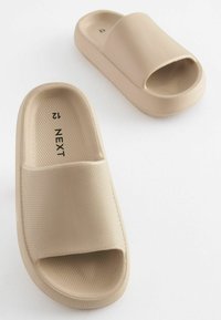 Beige slide-sandaler i tekstureret gummimateriale, åben tå-design og platformsål. Brandnavnet 'NEXT' synligt på indersiden af sålen.