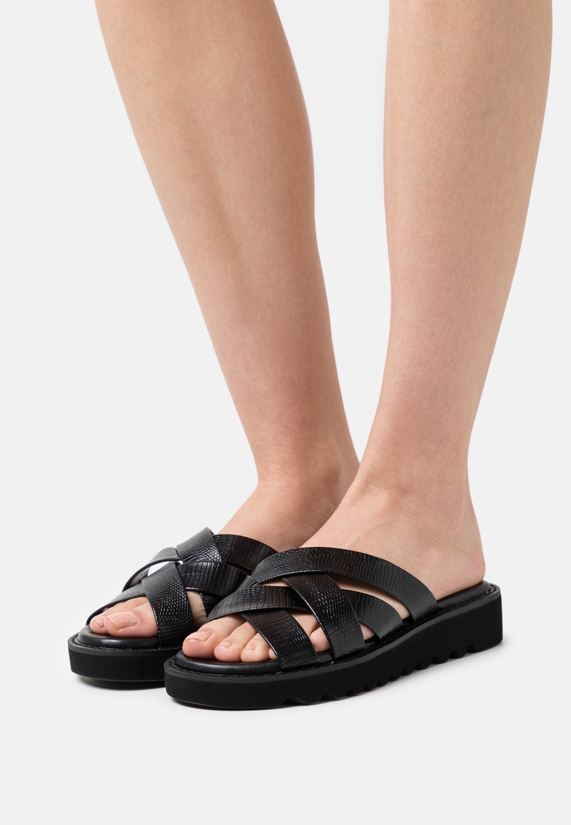 Sandales noires à glissière avec des brides texturées et croisées et une semelle épaisse et rainurée. Design ouvert à l'avant avec une finition lisse.