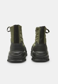 Botas de tobillo verdes y negras con parte superior de tela, cierre de cremallera y suela de goma texturizada con tacón acentuado y pestaña para tirar.
