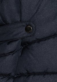 Giubbotto imbottito navy con finitura lucida e testurizzata, trapuntatura orizzontale e chiusura con bottoni a pressione neri.