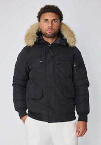 Veste rembourrée noire avec une capuche en fausse fourrure, des poches à fermeture éclair et à rabat, ainsi que des poignets côtelés. Texture lisse et design chaud.