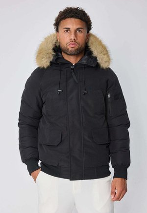 Veste rembourrée noire avec une capuche en fausse fourrure, des poches à fermeture éclair et à rabat, ainsi que des poignets côtelés. Texture lisse et design chaud.