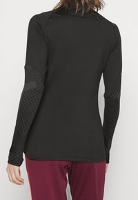 Schwarzes Langarmshirt mit strukturierten schwarzen Akzenten an den Ärmeln, taillierter Schnitt und glatter Stoff. Geschichteter Look am Saum.