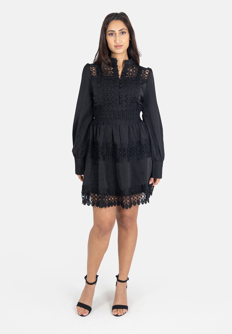 Zwarte jurk met lange mouwen, een hoge halslijn en ingewikkelde kantdetails bij het lijfje en de zoom. Uitlopende Silhouette met textielstructuur.