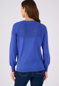 Pull bleu à manches longues avec un design en tricot texturé et à motifs dans le dos, corps uni et poignets et ourlet côtelés.