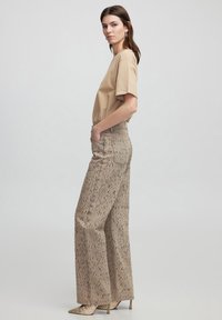Camiseta de algodón beige de manga corta combinada con pantalones beige de pierna ancha y cintura alta, con un patrón texturizado y moteado.