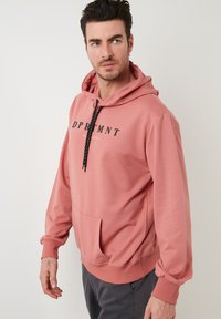 Felpa leggera rosa con cappuccio regolabile, dotata di tasca a marsupio frontale e logo stampato in nero. Tessuto morbido con polsini a coste.