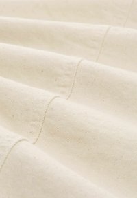 Naturstoff aus Baumwolle, off-white Farbton, mit einer strukturierten Oberfläche, die sichtbare Nähte und sanfte Falten aufweist, die Tiefe erzeugen.