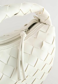 Sac à main blanc en tissage avec une surface texturée, doté d'une fermeture éclair et d'une anse tressée pour plus de détails.