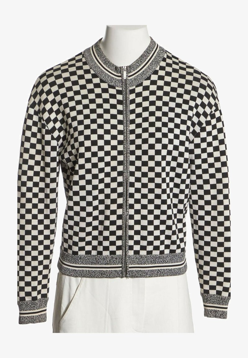 Veste zippée à carreaux noir et blanc avec col, poignets et ourlet côtelés présentant des détails rayés.