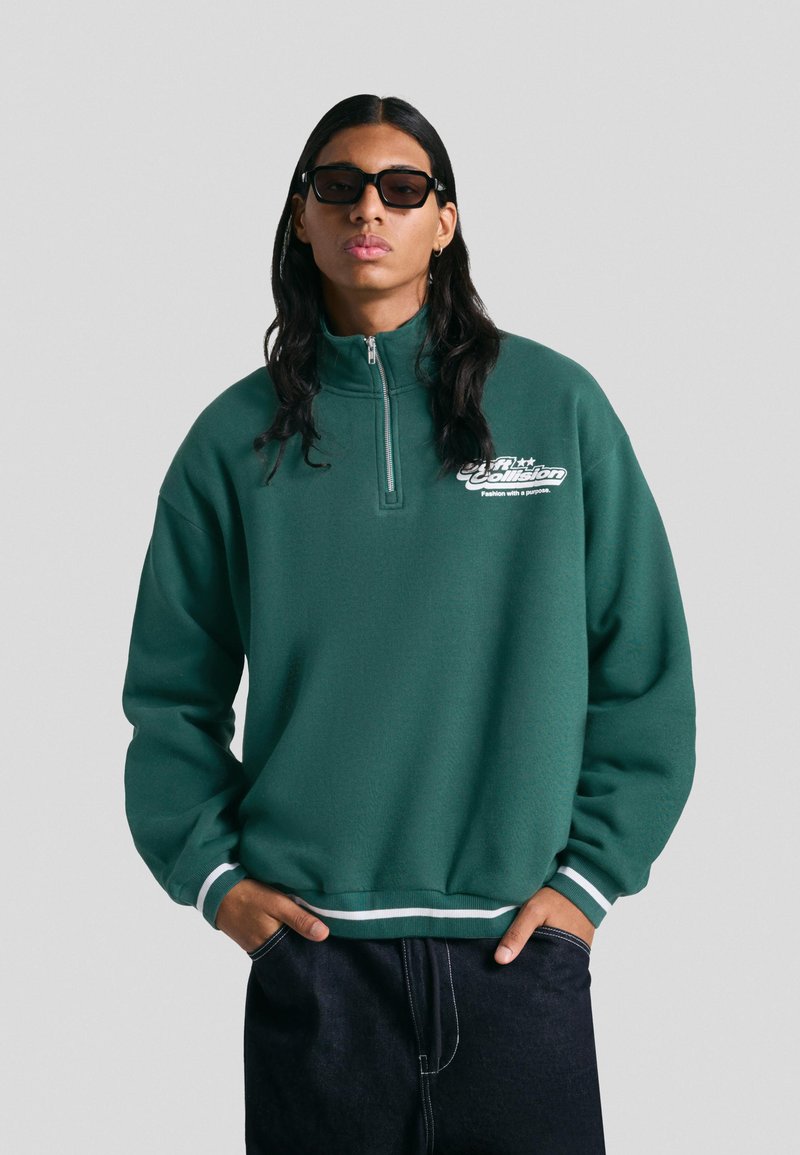 Pullover din fleece verde, cu fermoar la jumătate, cu accente albe, croială lejeră și un logo pe piept. Asortat cu pantaloni din denim închis.