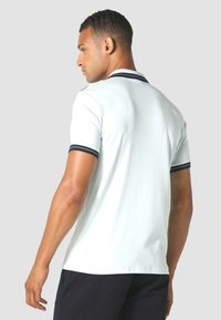 Gai zila polo krekls ar melnu apdari apkaklē un piedurknēs. Īsām piedurknēm, pieguļošs dizains, izgatavots no gludas kokvilnas auduma.