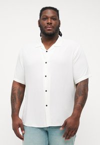 Short-sleeve white shirt made of smooth fabric, featuring a camp collar, front buttons, and contrasting black button accents.