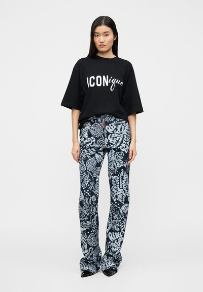 Μαύρο κοντομάνικο μπλουζάκι με τη λέξη "ICONique" σε λευκό. Σκούρο μπλε τζιν με λευκά μοτίβα σε στυλ γκράφιτι. Κομψά μαύρα τακούνια.