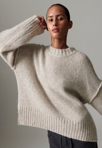 Sweater creme oversize feito de material de malha suave, com punhos e bainha canelados, decote redondo e detalhes texturizados.