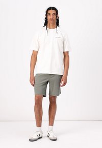 Hvid T-shirt med korte ærmer og et lille trykt logo, parret med strukturerede olivengrønne shorts og hvide sneakers med sorte striber.
