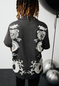 Svart t-shirt med kort ärm som har tryckta motiv av en vit drake och bläckfisk på baksidan, med en mjuk textur och avslappnad passform.