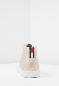 Zapatilla alta beige con parte superior de cuero texturizado, suela de goma blanca y un acento en la parte trasera de rayas rojas, blancas y azules.