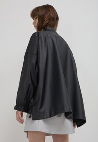 Giacca nera impermeabile con una vestibilità ampia, caratterizzata da una finitura lucida, polsini elastici e orlo con coulisse per una regolazione ottimale.
