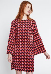 Rode en zwarte jurk met belmouwen, met een geometrisch patroon van overlappende halve cirkels in tinten rood en roze.