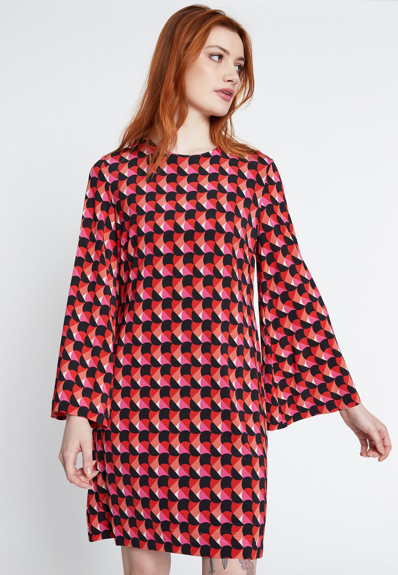 Rode en zwarte jurk met belmouwen, met een geometrisch patroon van overlappende halve cirkels in tinten rood en roze.