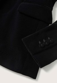 Manche de manteau noire avec trois boutons noirs assortis et un revers plié visible sur fond blanc.