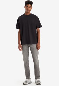 Black short-sleeve T-shirt with a crew neck, paired with light gray jeans and gray sneakers featuring white accents.