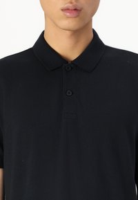 Camisa polo preta com colarinho, placket de dois botões e logótipo bordado. Tecido de algodão com uma textura fina e design ajustado.