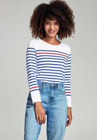 Wit overhemd met lange mouwen en blauwe en rode horizontale strepen, gecombineerd met lichtblauwe jeans. De stof lijkt zacht te zijn met een casual pasvorm.
