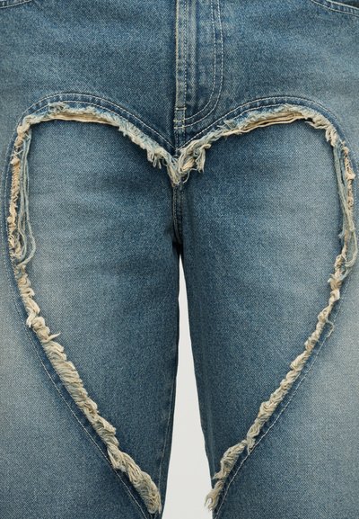 Τζιν παντελόνια με καρδιά κόψιμο στα γόνατα, με ξεφτισμένα άκρα, ξεθωριασμένο μπλε χρώμα και τραχιά υφή.