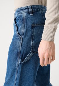 Vaqueros de mezclilla con un lavado azul oscuro, que presentan una cintura ajustada, bolsillos laterales y detalles de costura únicos a lo largo de las costuras y los bolsillos.